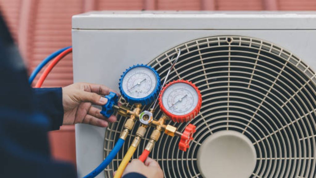 HVAC technician checking refrigerant pressure with a manifold gauge set connected to an outdoor air conditioning condenser unit.